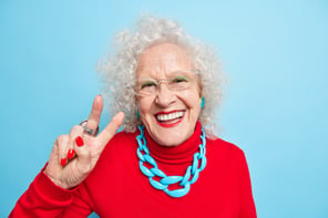 portrait-cheerful-nice-looking-elderly-woman-smiles-happily-makes-peace-gesture-shows-v-sign-dressed-red-jumper-with-necklace-expresses-positive-emotions